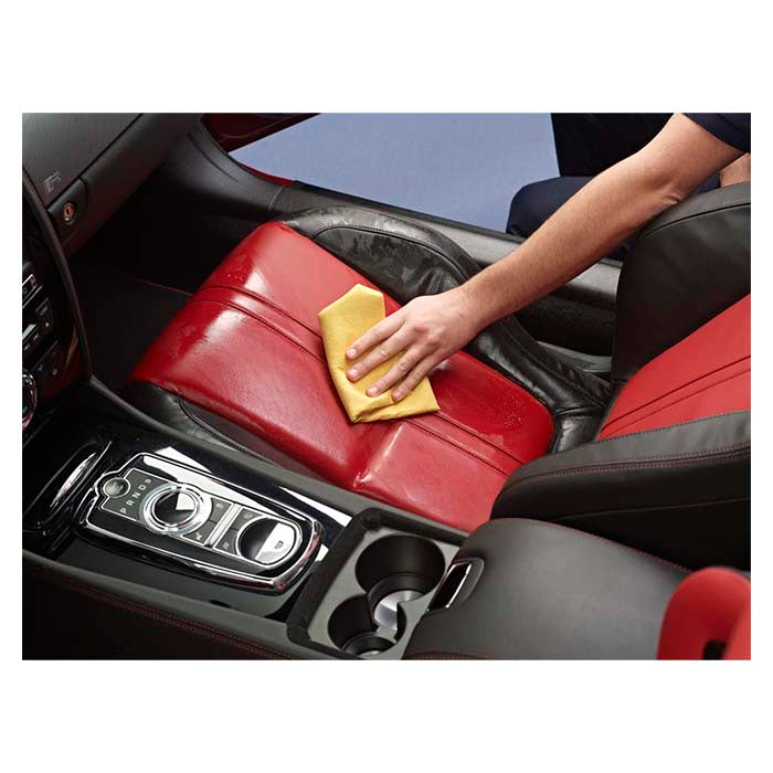Person rengør bilens røde læderkabine med en gul klud og læderrens.