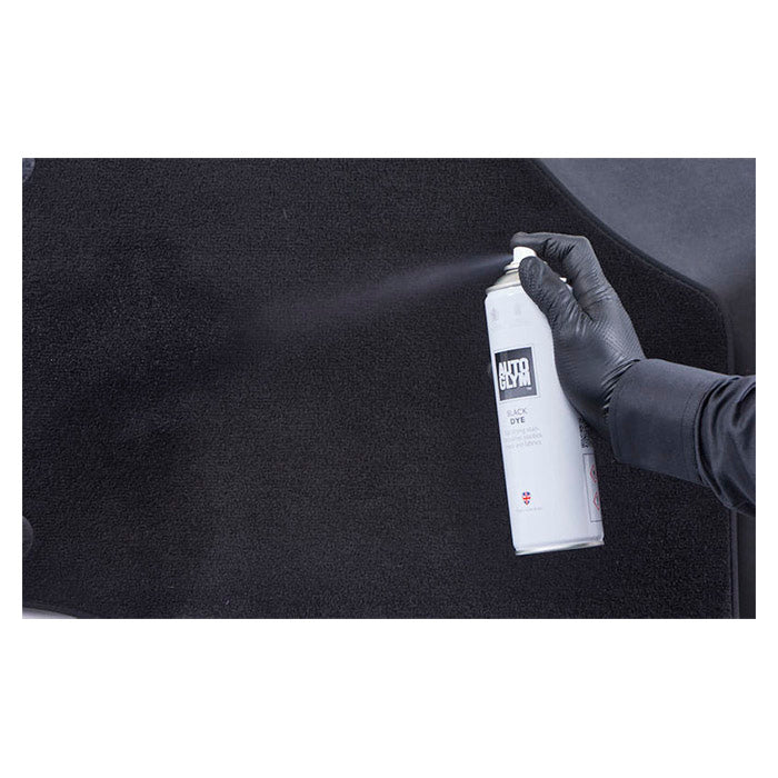 Hånd med handske sprayer Autoglym Black Dye tekstilspray på sort bilmåtte.