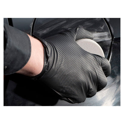 Hånd iført sort handske polerer ridser på bilens lak med skumapplikator