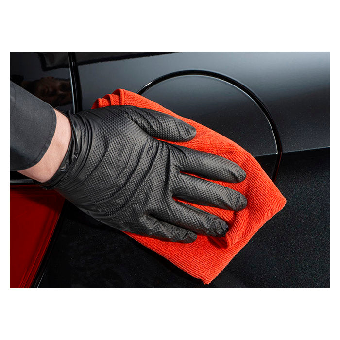 Hånd med handske polerer bilens sorte lak med mikrofiberklud