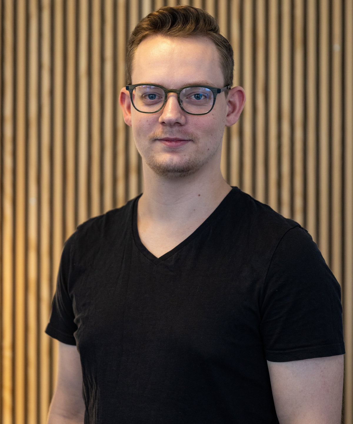 Medarbejder med briller i sort t-shirt, et venligt ansigt, klar til at hjælpe.